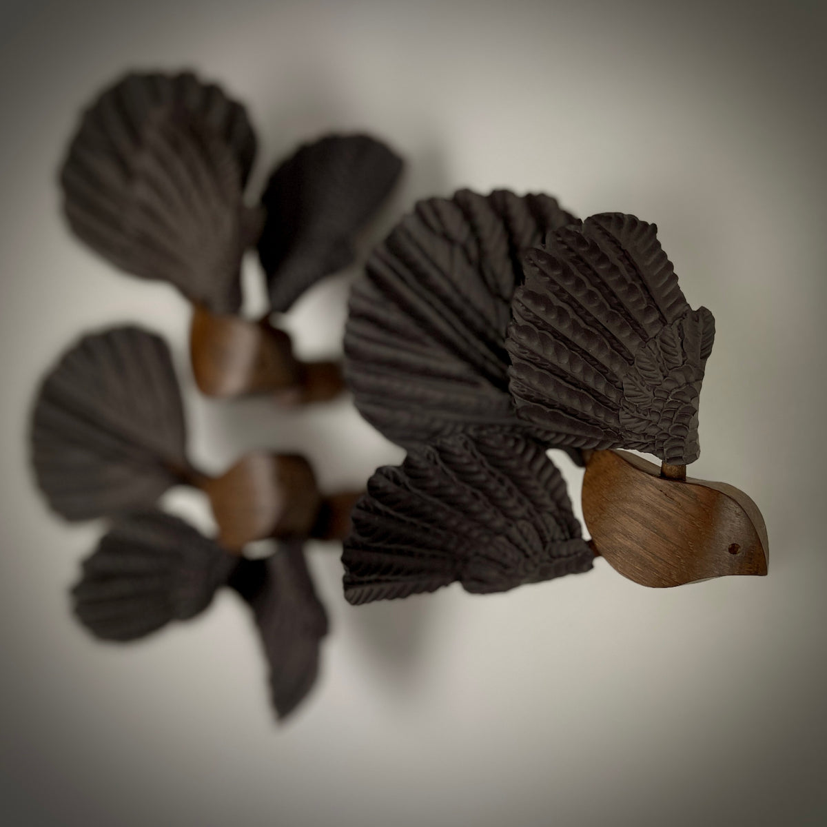Close-up of Pīwakawaka sculptures by Tim Main, showing an oak body and textured black stoneware wings and tail.