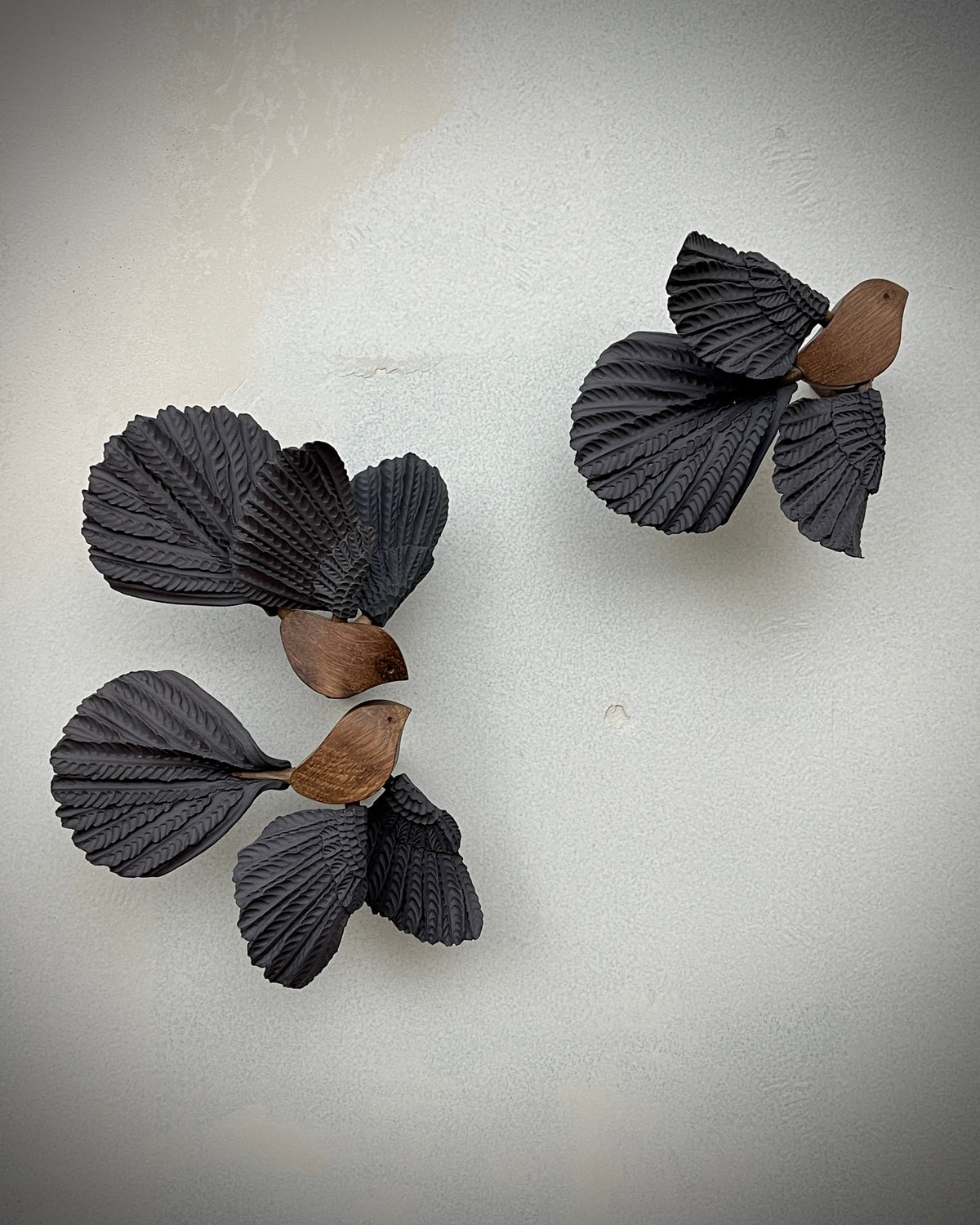 Three Pīwakawaka fantail sculptures by Tim Main, with oak bodies and black stoneware wings and tails, on a pale wall.